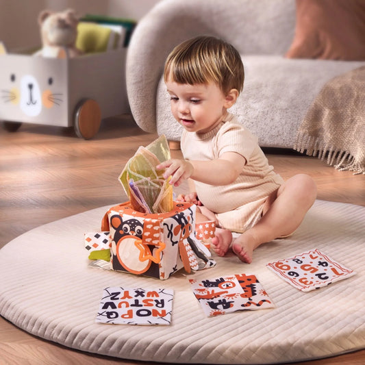 Baby playing with high-contrast black and white sensory tissue box toy and fabric cards for early learning and visual development in a cozy nursery