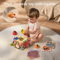 Baby playing with a Montessori tissue box toy and fruit squeeze toys that make sounds, surrounded by colorful animal flash cards and soft sensory tissues, designed for early childhood sensory and motor skill development.