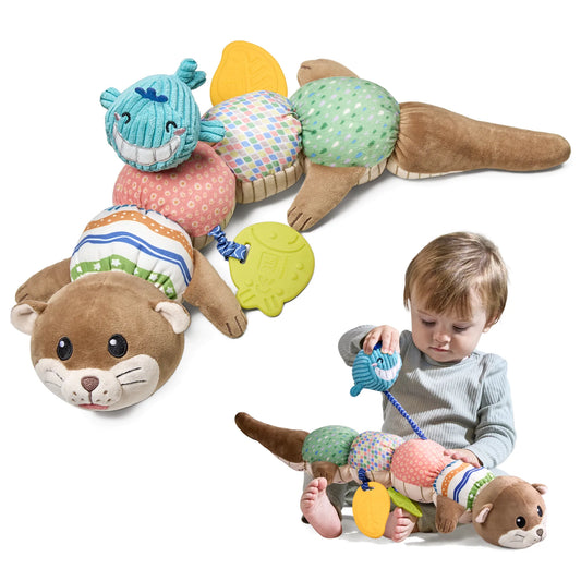 Colorful baby sensory toy designed as a plush otter in caterpillar form. The toy features a brown otter head with cute facial details at one end and a tail at the other, with five colorful textured segments in between. Each segment has different patterns and fabrics: pink with small circles, striped, multicolored squares, green with dots, and a blue whale head attachment. Yellow leaf-shaped teethers hang from the toy. 