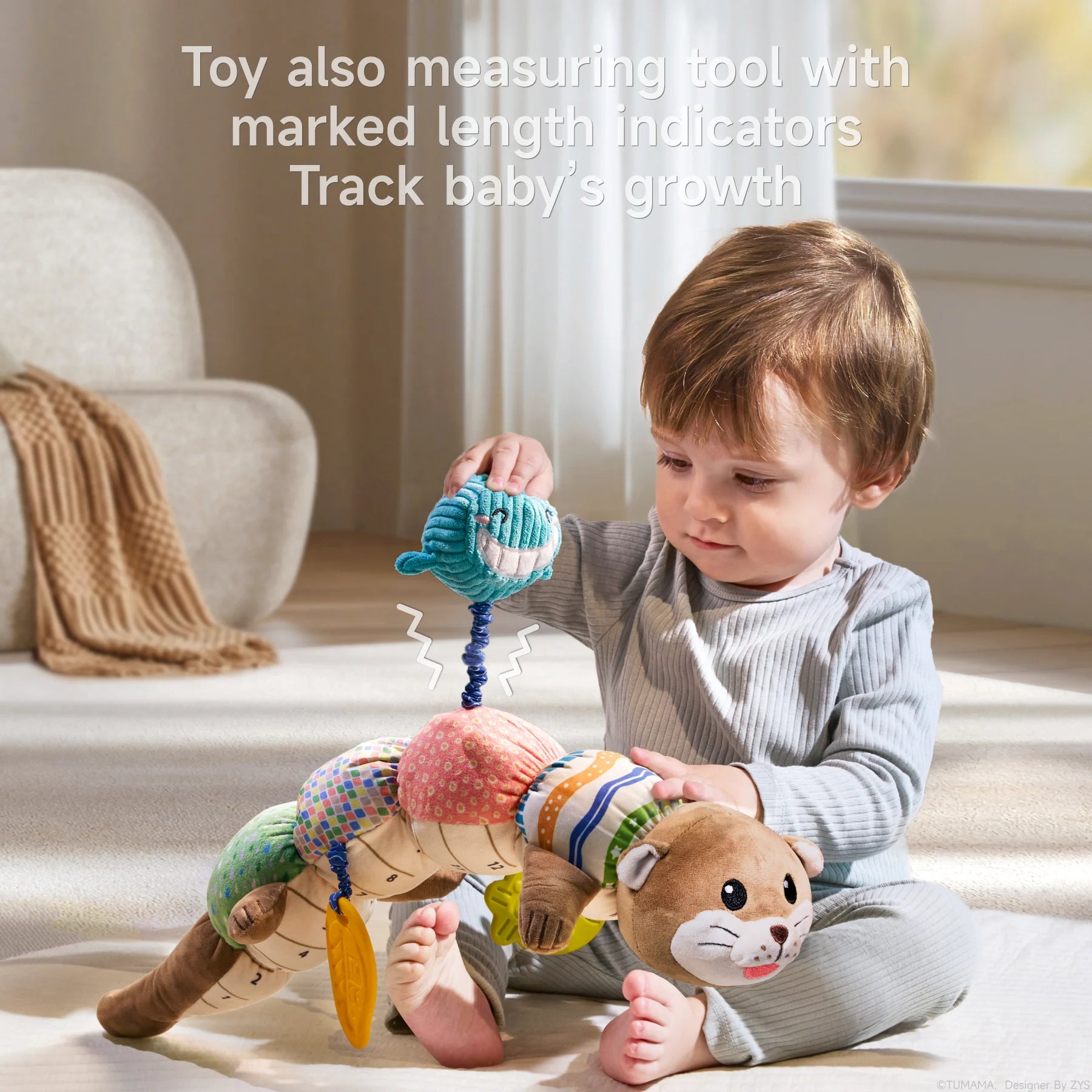 A toddler in light gray ribbed clothing sits on a cream-colored carpet, engaging with a multifunctional otter sensory toy. The child is pulling on the blue whale teether that extends on a coiled cord from the toy's body. The plush toy features a cute brown otter head with whiskers and eyes on one end, and a tail on the other, with five colorful segments in between (green dotted, multicolored squares, pink with circles, and striped patterns). Yellow leaf-shaped teethers hang from the toy. Text overlay at the