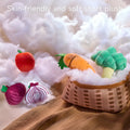 A group of plush felted vegetable toys is arranged on a soft, cloud-like textured surface. A brown and white checkered basket holds a green strawberry and a green broccoli, and a label on the image reads 