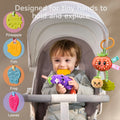 A baby seated in a stroller holding a cute eggplant toy with a fish-shaped teether. The toy set includes colorful, textured teethers in shapes like pineapple, fish, frog, and leaves, designed for tiny hands to hold and explore.