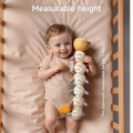 Smiling baby lying in a crib holding a plush caterpillar toy with a built-in height measurement scale; text overlay indicates the maximum measurable height is 43 cm.